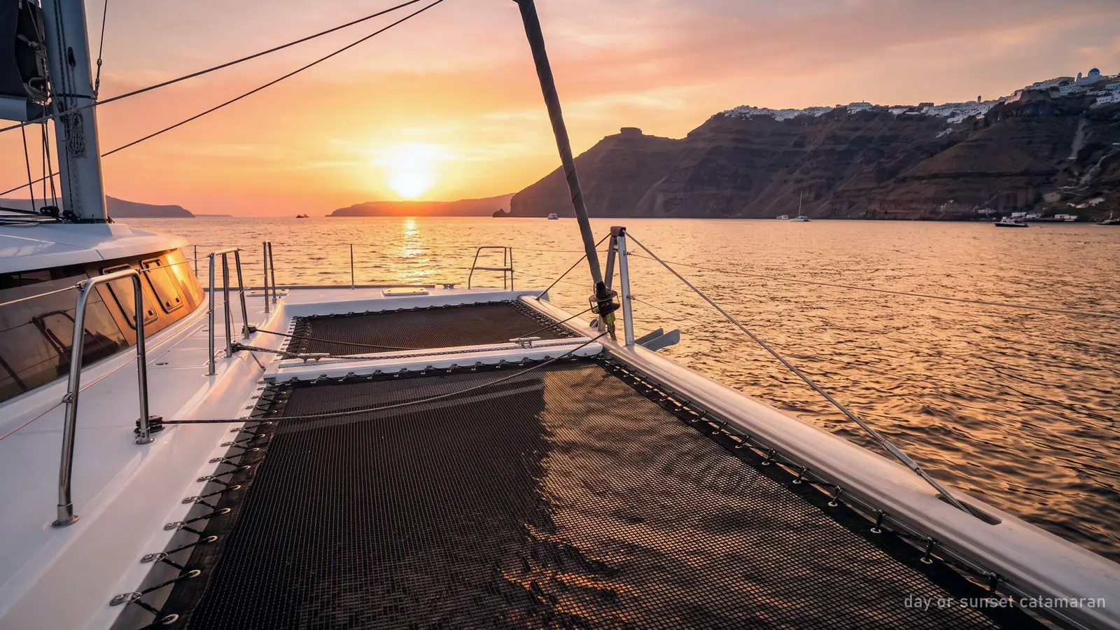 The netting deck of a catamaran in the Santorini caldera as the sun sets over the sea